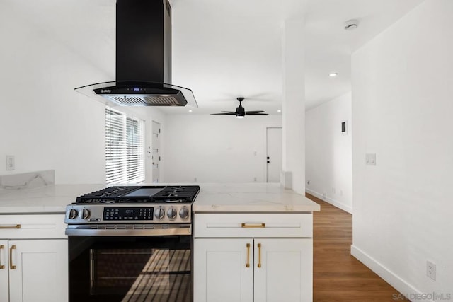 kitchen with stainless steel range with gas stovetop, light stone counters, white cabinets, and island range hood