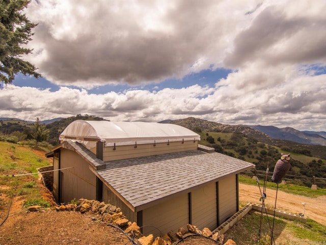 view of property exterior featuring an outbuilding, roof with shingles, and a mountain view