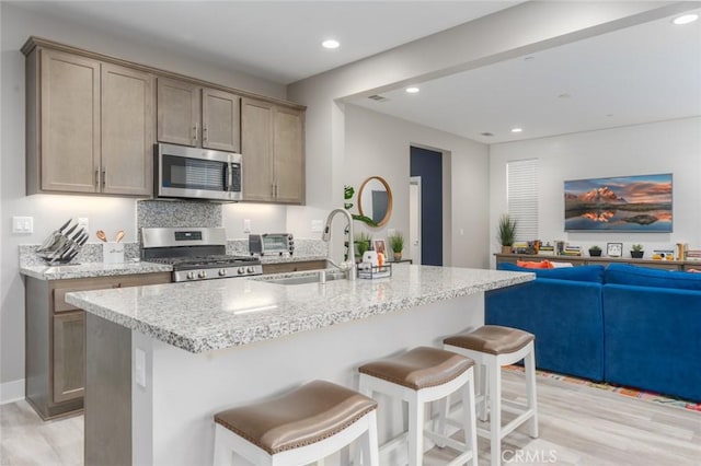 kitchen with a kitchen breakfast bar, light hardwood / wood-style flooring, light stone countertops, an island with sink, and stainless steel appliances