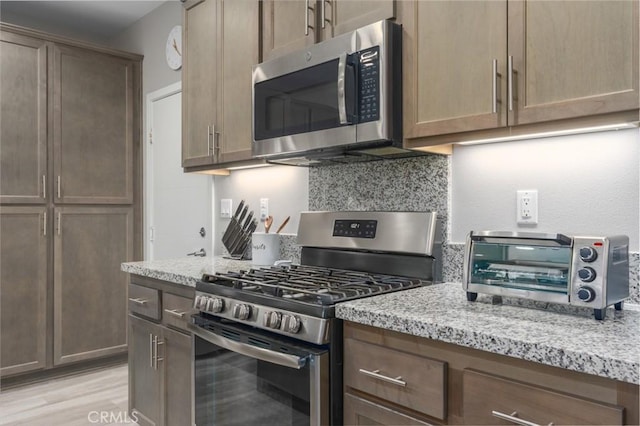 kitchen with light stone countertops, light hardwood / wood-style floors, and appliances with stainless steel finishes