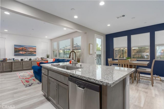 kitchen featuring stainless steel dishwasher, light hardwood / wood-style flooring, sink, light stone counters, and a kitchen island with sink