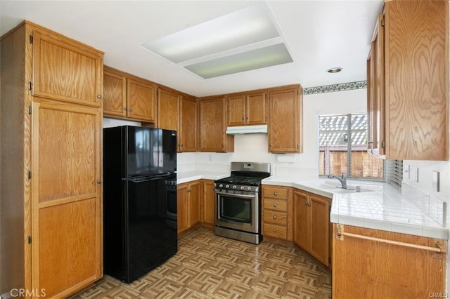 kitchen featuring black refrigerator, sink, light parquet flooring, stainless steel gas range, and tile counters