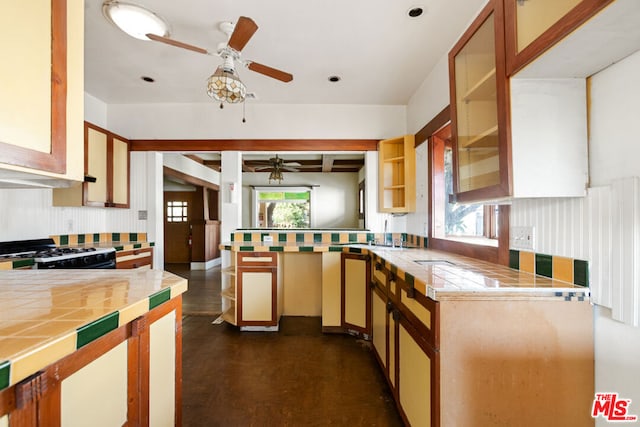 kitchen featuring kitchen peninsula, ceiling fan, beam ceiling, range with gas cooktop, and tile counters