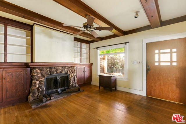 unfurnished living room featuring ceiling fan, dark hardwood / wood-style floors, beamed ceiling, and a fireplace