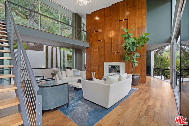 living room featuring a wall of windows, a towering ceiling, wooden walls, wood-type flooring, and a chandelier