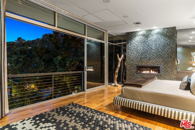 bedroom featuring hardwood / wood-style flooring, a large fireplace, and a wall of windows