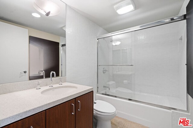 full bathroom featuring vanity, toilet, tile patterned flooring, and combined bath / shower with glass door