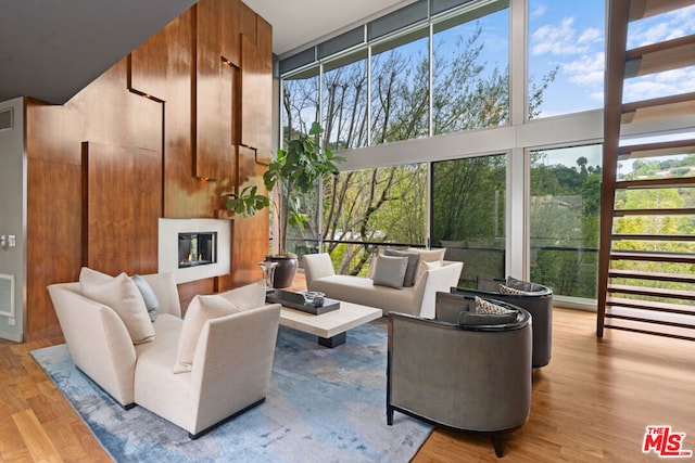 living room with a towering ceiling, a wall of windows, plenty of natural light, and hardwood / wood-style flooring