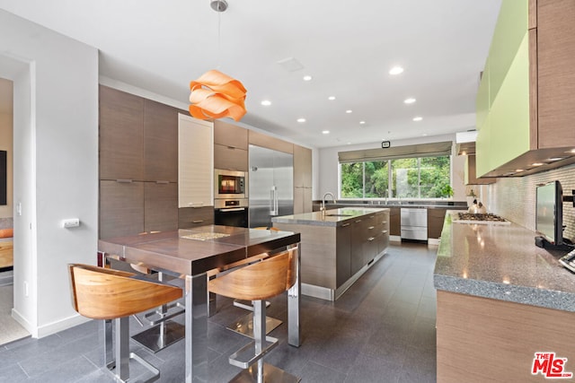 kitchen featuring sink, backsplash, built in appliances, an island with sink, and decorative light fixtures