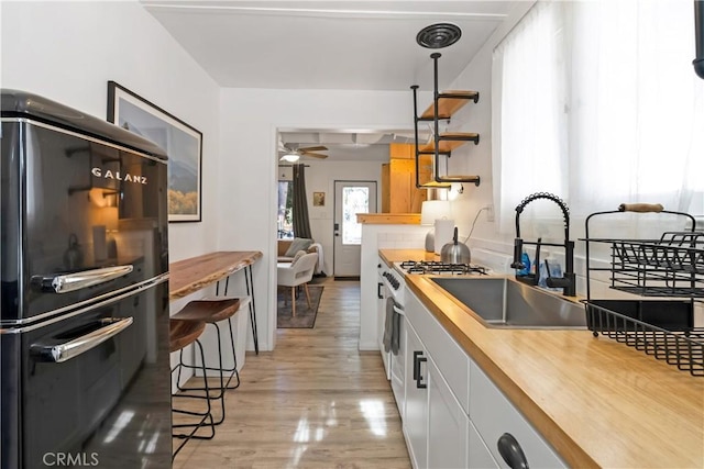 kitchen with black refrigerator, white cabinetry, butcher block counters, sink, and hanging light fixtures