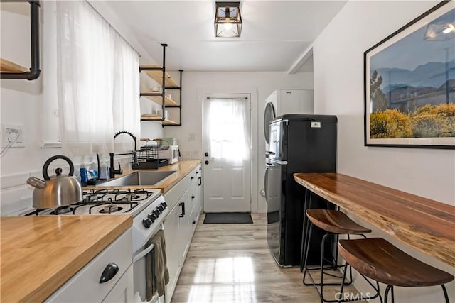 kitchen featuring white cabinets, sink, hanging light fixtures, black fridge, and white range with gas stovetop