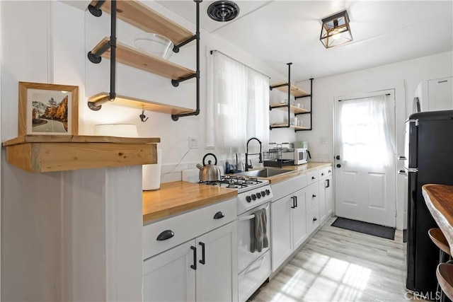 kitchen with sink, light wood-type flooring, white cabinets, butcher block countertops, and white appliances