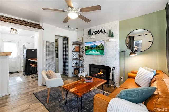 living room featuring a brick fireplace, light hardwood / wood-style flooring, and ceiling fan