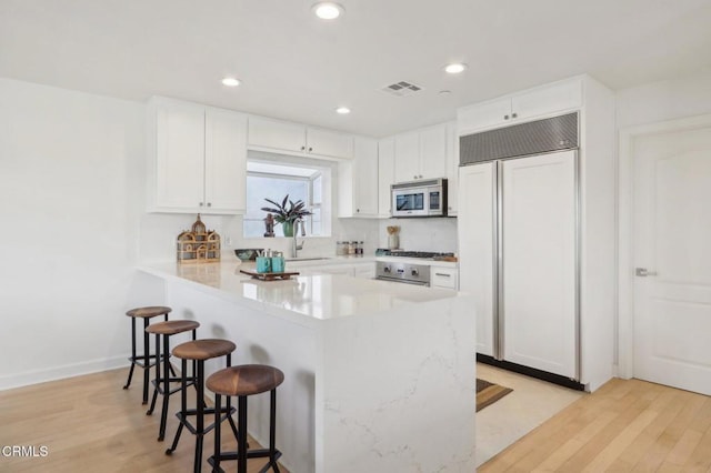 kitchen with appliances with stainless steel finishes, a kitchen breakfast bar, white cabinets, light wood-type flooring, and sink