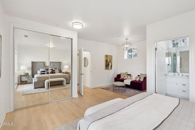 bedroom with a closet, a chandelier, ensuite bath, baseboards, and light wood-style floors