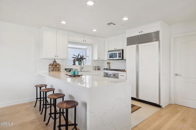 kitchen with white cabinets, a kitchen bar, light wood finished floors, and paneled refrigerator