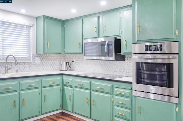 kitchen with sink, backsplash, green cabinetry, and appliances with stainless steel finishes