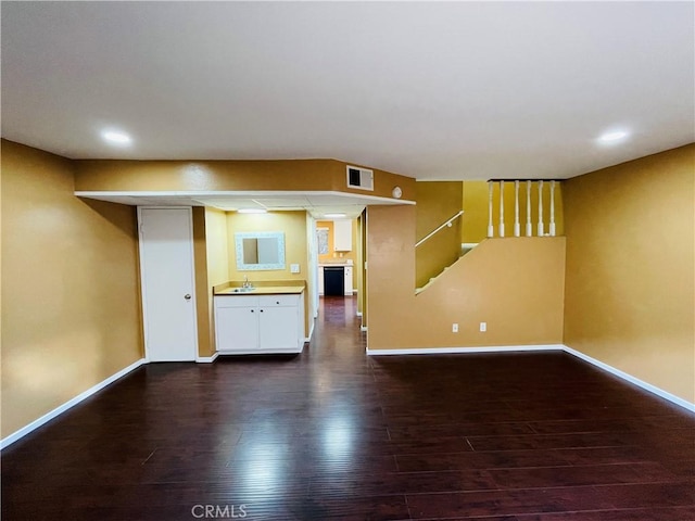 unfurnished living room featuring dark wood-style floors, a sink, visible vents, and baseboards