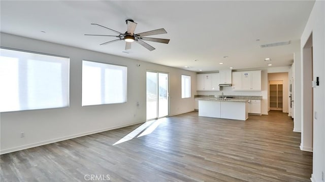 interior space with hardwood / wood-style flooring, white cabinets, a center island with sink, and ceiling fan