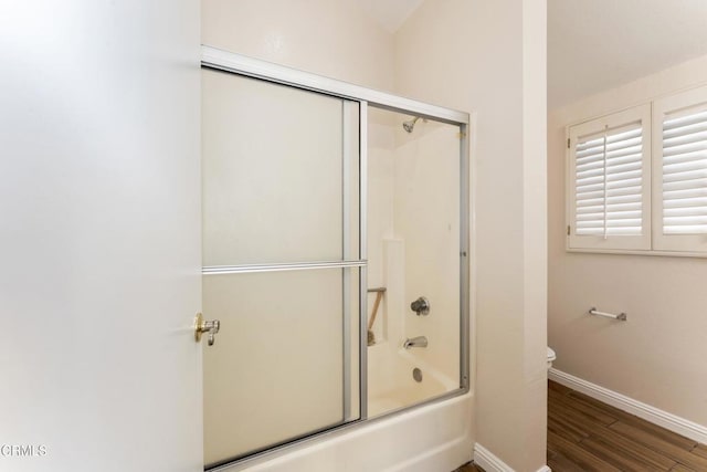 bathroom featuring wood-type flooring, toilet, and combined bath / shower with glass door