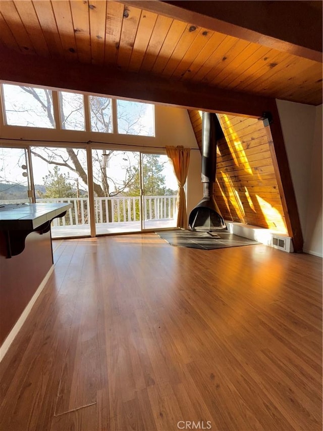 unfurnished living room featuring wood-type flooring, a water view, beam ceiling, a wood stove, and wooden ceiling