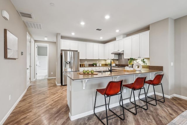 kitchen with stainless steel refrigerator with ice dispenser, white cabinetry, sink, kitchen peninsula, and a breakfast bar area