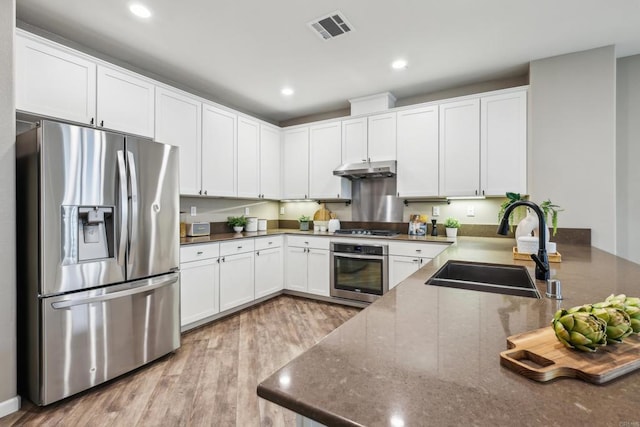 kitchen featuring white cabinetry, stainless steel appliances, dark stone countertops, sink, and light hardwood / wood-style flooring