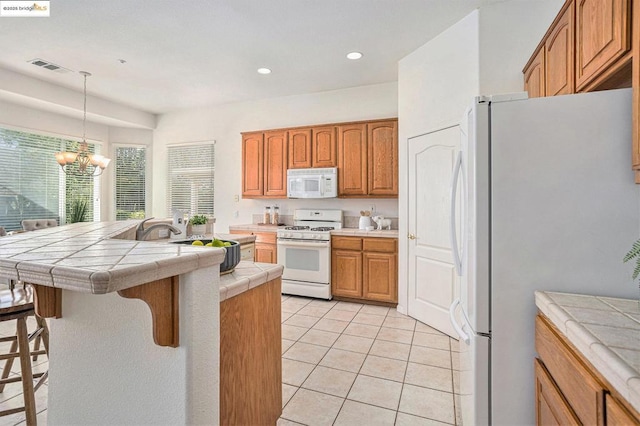 kitchen featuring white appliances, pendant lighting, a kitchen bar, tile countertops, and light tile patterned flooring