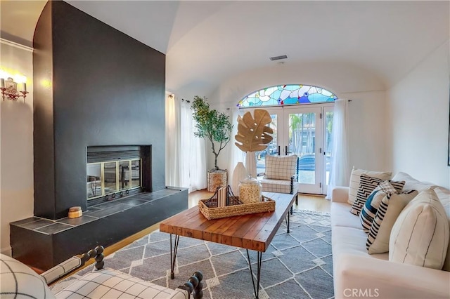 living room with hardwood / wood-style flooring, a tiled fireplace, vaulted ceiling, and french doors