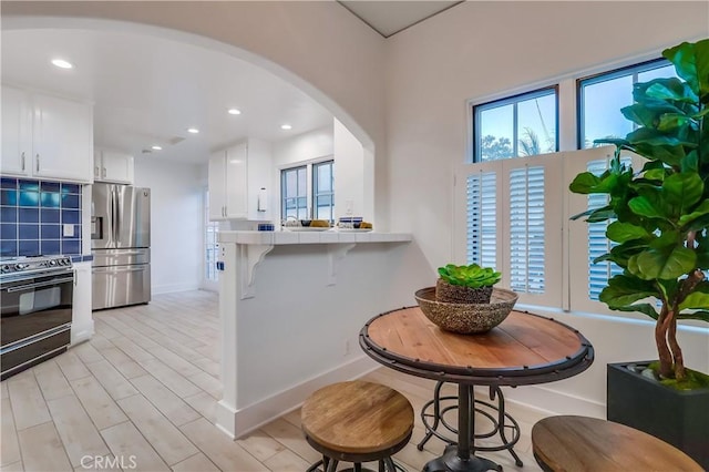 kitchen with white cabinets, a kitchen breakfast bar, tile counters, stainless steel fridge with ice dispenser, and black / electric stove