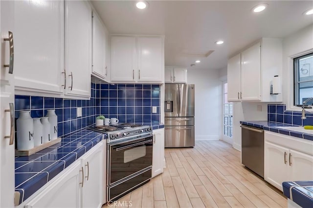 kitchen featuring white cabinetry, backsplash, tile countertops, and appliances with stainless steel finishes