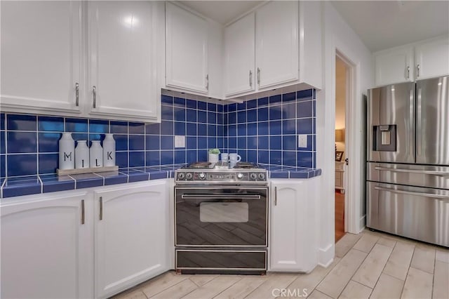 kitchen featuring tasteful backsplash, white cabinetry, range, tile counters, and stainless steel fridge with ice dispenser