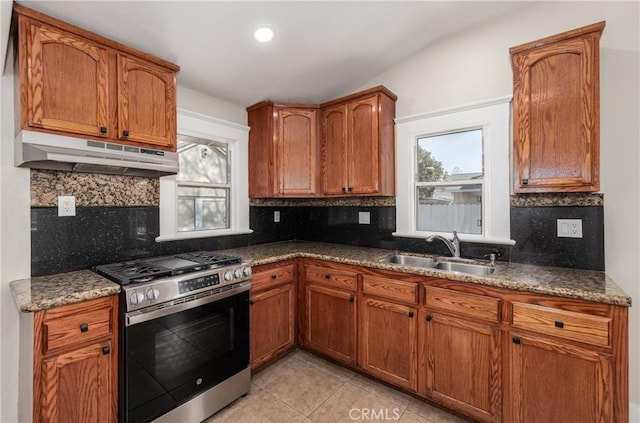 kitchen featuring gas range, sink, backsplash, light tile patterned floors, and dark stone counters