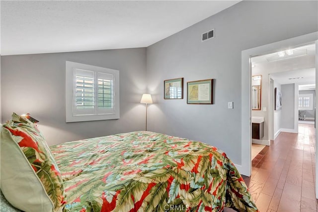 bedroom featuring ensuite bath, hardwood / wood-style floors, and lofted ceiling