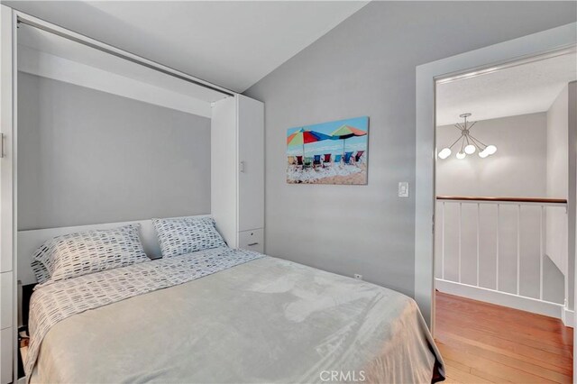 bedroom featuring wood-type flooring, a chandelier, and vaulted ceiling