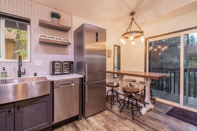 kitchen featuring light hardwood / wood-style floors, appliances with stainless steel finishes, sink, pendant lighting, and backsplash