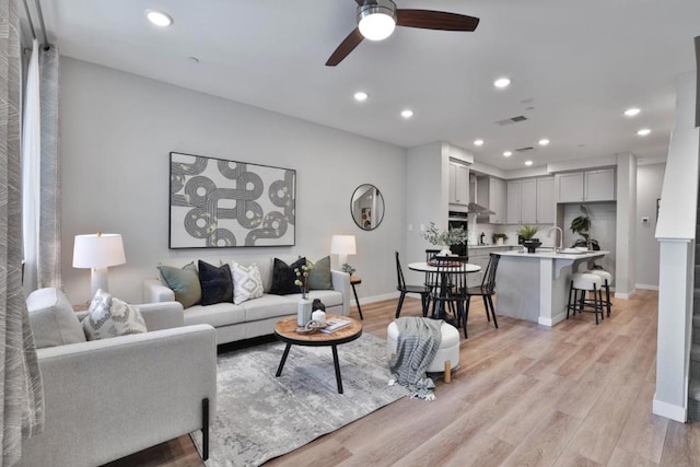 living room featuring ceiling fan, sink, and light hardwood / wood-style floors