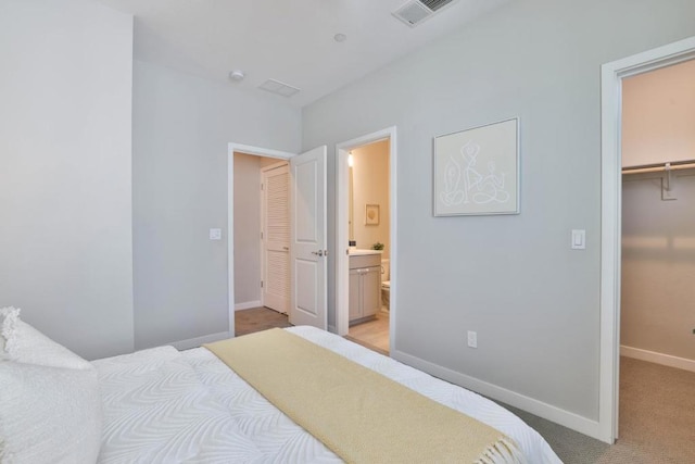 bedroom with a closet, a walk in closet, light colored carpet, and ensuite bath