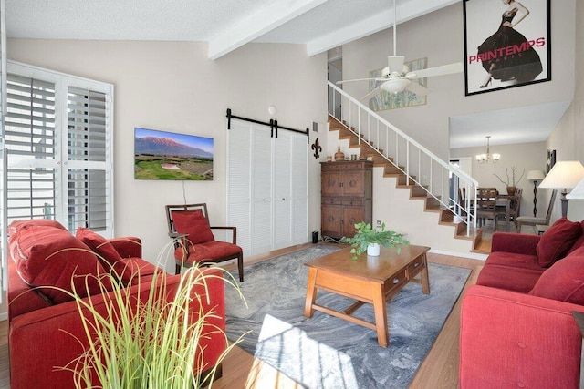 living room with ceiling fan with notable chandelier, wood-type flooring, lofted ceiling with beams, and a barn door