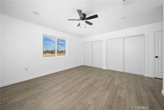 unfurnished bedroom featuring ceiling fan, hardwood / wood-style floors, and multiple closets