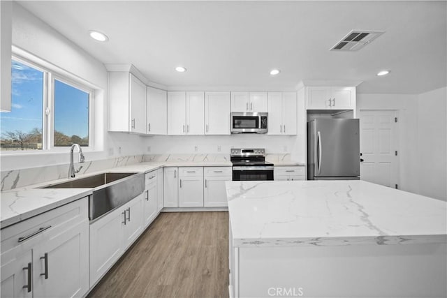 kitchen with light stone countertops, appliances with stainless steel finishes, white cabinetry, sink, and light hardwood / wood-style flooring