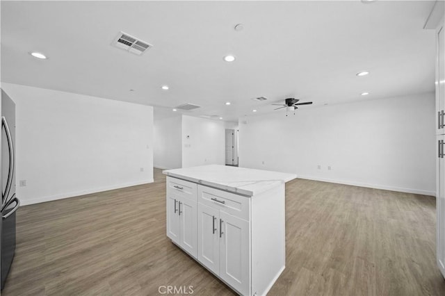 kitchen with a kitchen island, white cabinetry, light hardwood / wood-style flooring, and light stone countertops