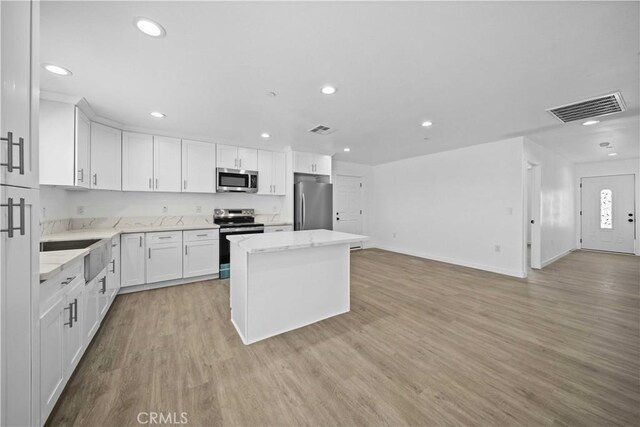 kitchen with white cabinetry, a center island, stainless steel appliances, and light hardwood / wood-style flooring