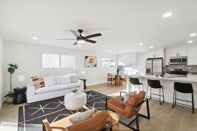 living room with ceiling fan, sink, and light wood-type flooring