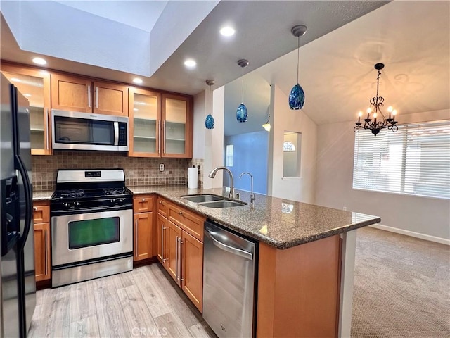 kitchen featuring kitchen peninsula, hanging light fixtures, appliances with stainless steel finishes, sink, and dark stone counters