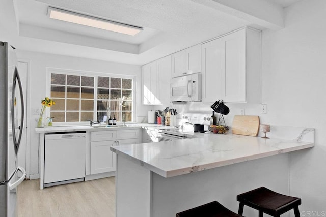 kitchen with kitchen peninsula, white cabinetry, light stone counters, a breakfast bar, and stainless steel appliances