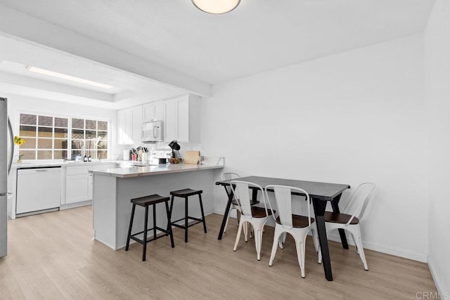 kitchen featuring white appliances, a kitchen bar, white cabinets, light hardwood / wood-style flooring, and kitchen peninsula