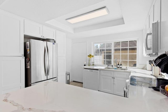 kitchen featuring white cabinets, sink, stainless steel fridge, a raised ceiling, and white dishwasher