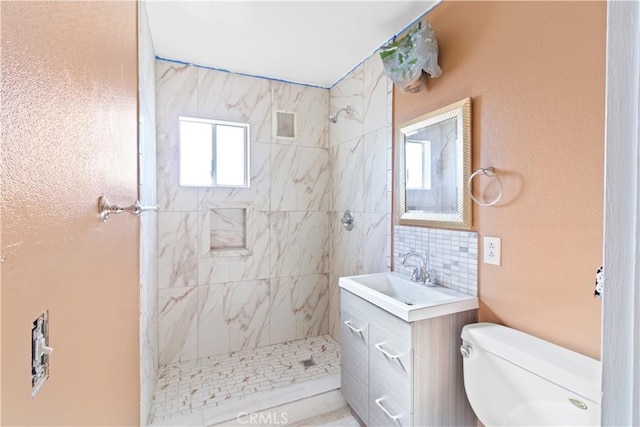 bathroom featuring backsplash, toilet, vanity, and a tile shower