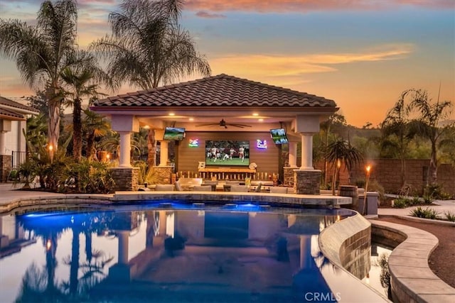 pool at dusk featuring a gazebo, a patio, and ceiling fan